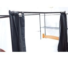 two black curtains are hanging from the side of a rack with clothes on it and one is closed