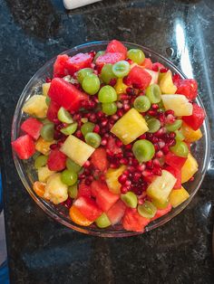 a glass bowl filled with fruit on top of a black granite countertop next to a knife and fork