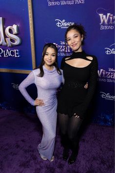 two women standing next to each other on a purple carpet