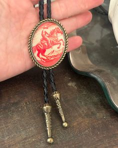 This awesome bolo tie has a vintage cowboy print with a clear resin coating and metal backing. Handmade in our shop! The cord is black and genuine leather. Our bolos pair nicely with many of our belt buckles! They make wonderful gifts.    The western bolo tie rope length is 39' ;  pendant size is 1 1/2'' x 1 1/4'' Cowboy Tie, Cowboy Accessories, Western Bolo Tie, Cowboy Print, Boy Vintage, Rodeo Horses, Cowboy Belt, Bolo Ties, Mens Necklace