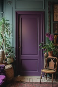 a purple door with potted plants in the corner and a chair next to it