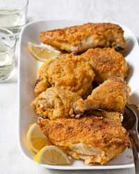 fried chicken with lemon wedges in a white serving dish next to glasses of water