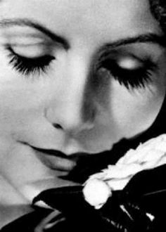 a black and white photo of a woman with long eyelashes holding a flower in her hand