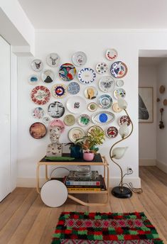 a white room with plates on the wall and a table in front of it that has a lamp next to it