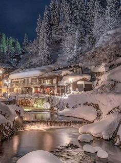 a river running through a snow covered forest next to a building with lights on at night