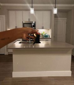 a person is reaching for something on the counter top in a kitchen with white cabinets and stainless steel appliances