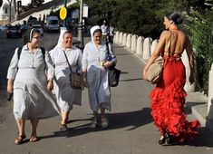 three women walking down the street in dresses and head coverings, one wearing a red dress