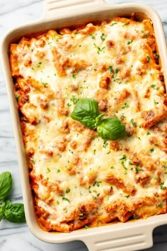 a casserole dish with meat and cheese in it, garnished with fresh basil