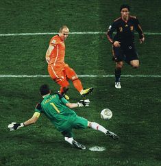 two men playing soccer on a field with one kicking the ball while another tries to block it