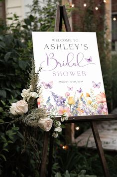 a welcome sign for a bridal shower with flowers on it and lights in the background