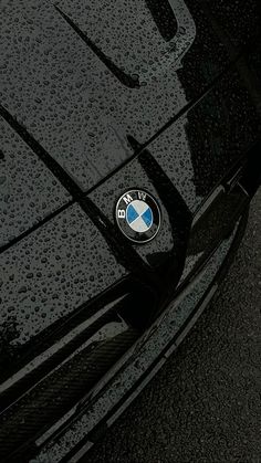 the front end of a black bmw car with water droplets on it's hood