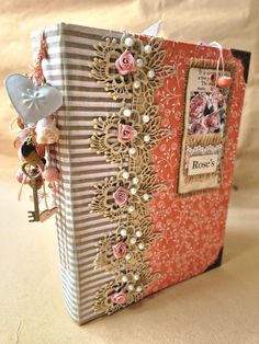 This elegant rose inspired journal is made with a hard cover, adorned with fabric, patterned paper, a layered embelishment, metal book corners and an intricate lace trim.  The spine has a charm made with an eclectic mix of beads, buttons and other treasures.  Inside consists of old book pages, beautiful patterned papers, velum and sheet music.  All three signatures contain an array of pockets, tuck spots, ephemera and lace trims.  The journal also has an elasticated closure allowing for plenty of room for your photos, treasures and memories. The journal measures 18 x 25cm / 7 1/4 x 9 1/4 inch (approx) 3 Signatures - 76 pages Handmade Rose, Book Corners, Old Book Pages, Lace Trims, The Journal, Patterned Paper, Blank Book