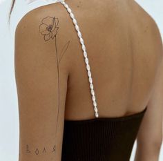 the back of a woman's shoulder with a single flower tattoo on her left arm