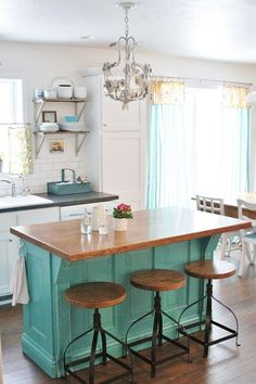 an island in the middle of a kitchen with three stools and a chandelier