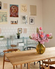 a wooden table topped with a vase filled with flowers next to pictures on the wall