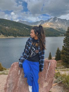 a woman sitting on top of a rock next to a lake