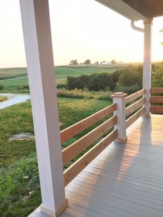 a porch with wooden railings and grass on the other side, overlooking an open field