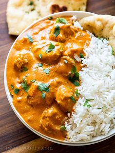 a bowl filled with rice and meat next to naan bread on a wooden table