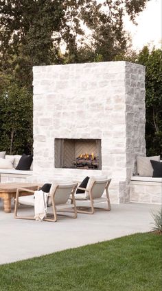 an outdoor fireplace in the middle of a patio with chairs around it and a table next to it