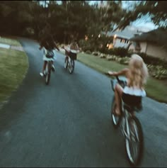 three people riding bikes down a street with houses in the background and trees on either side