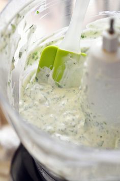 a food processor filled with white sauce and a green blender attachment in the middle