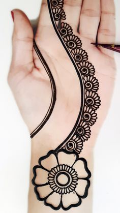 a woman's hand with a henna tattoo design on it and a pen in the other hand