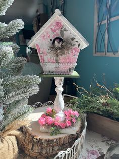 there is a bird house on top of a tree stump with pink flowers in the foreground