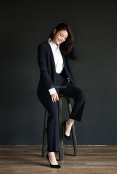 a woman sitting on top of a stool wearing a black suit and white shirt with high heels