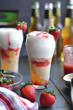 two glasses filled with ice cream and strawberries on top of a table next to bottles