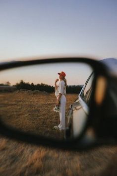 a woman standing next to a car with her reflection in the side view mirror on it