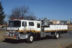 a white fire truck driving down a street next to a tree and grass covered field