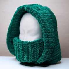 a white mannequin head wearing a green knitted hat on top of a table