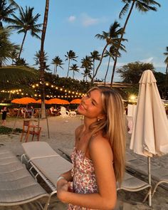 a woman standing on the beach next to chairs and umbrellas with palm trees in the background