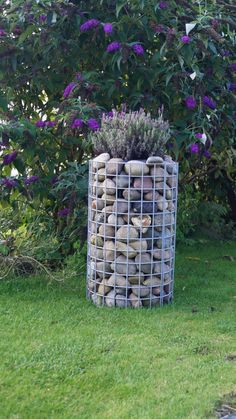 a large metal container filled with rocks in the middle of a grass covered yard next to purple flowers