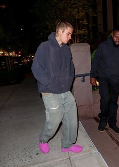 two men walking down the sidewalk at night, one wearing pink shoes and the other in black