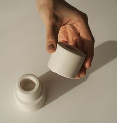 a hand holding a cup over a white surface with a small object in the foreground