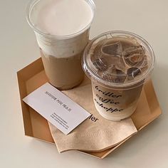 two cups of coffee sitting on top of a brown tray next to a paper card