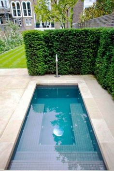 an empty swimming pool in the middle of a yard with hedges on either side and a blue tile floor