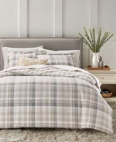 a bed with plaid comforter and pillows in a white room next to a plant