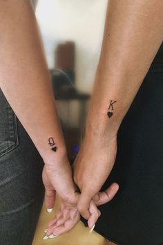 two people holding hands with small tattoos on their arms and the other hand behind them