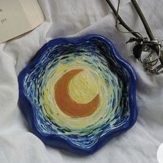 a blue bowl sitting on top of a white cloth covered table next to an open book