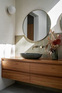 a bathroom sink sitting under a round mirror next to a vase with flowers in it