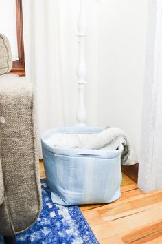 a dog bed sitting on top of a wooden floor next to a chair and lamp