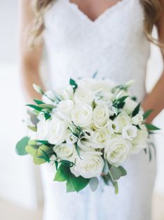 a bridal holding a bouquet of white roses and greenery on her wedding day