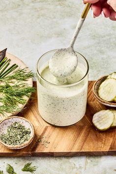 a person spooning something out of a jar with cucumbers on the side