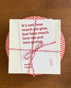 a gift wrapped in red and white paper with a quote on it sitting on top of a wooden table