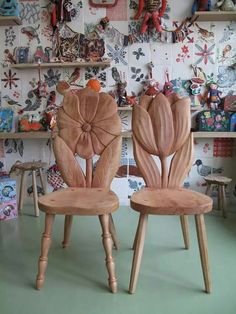 two wooden chairs sitting side by side in front of a wall with pictures on it