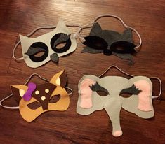 four masks are sitting on a wooden table, one has an elephant mask and the other has a fox mask