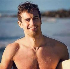 a shirtless man holding a surfboard on the beach