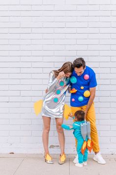 a man and woman standing next to a little boy in front of a white brick wall